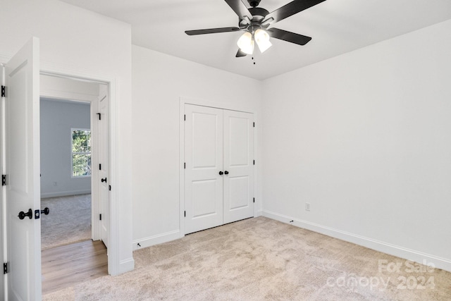 unfurnished bedroom with a closet, light colored carpet, and ceiling fan