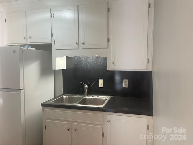 kitchen with white refrigerator, white cabinetry, and sink