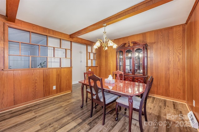 dining space featuring hardwood / wood-style floors, beam ceiling, a notable chandelier, and wooden walls