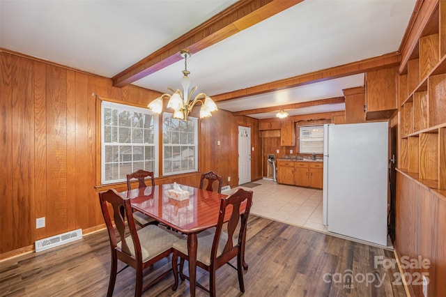 dining room with beam ceiling, wood walls, an inviting chandelier, and light hardwood / wood-style flooring