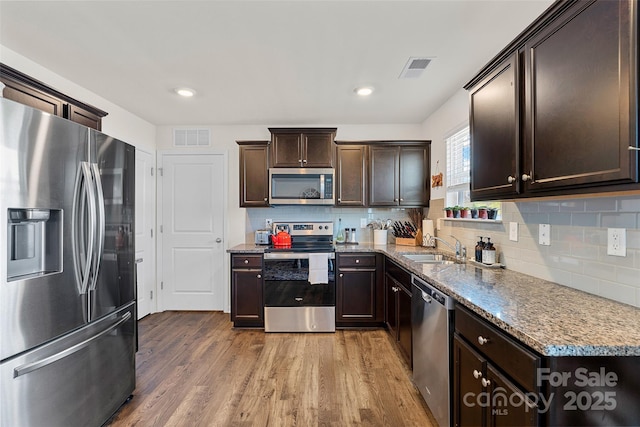 kitchen featuring light stone counters, dark brown cabinetry, stainless steel appliances, sink, and hardwood / wood-style floors