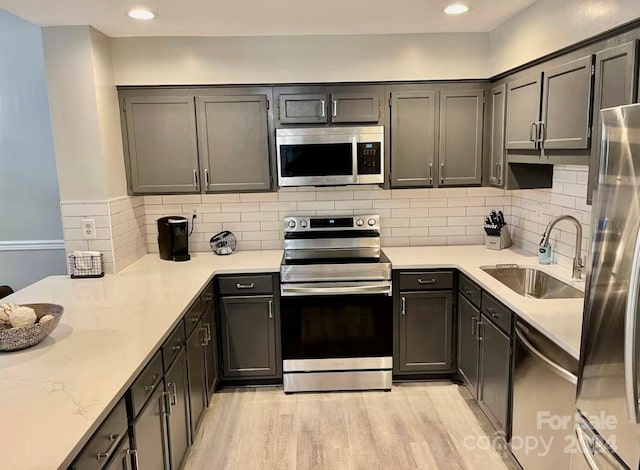 kitchen with backsplash, sink, light stone countertops, light wood-type flooring, and stainless steel appliances