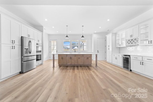 kitchen featuring stainless steel appliances, beverage cooler, hanging light fixtures, and white cabinets