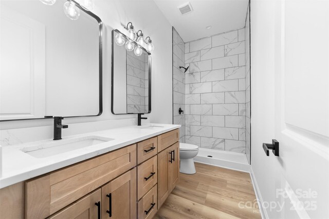 bathroom with a tile shower, vanity, hardwood / wood-style floors, and toilet