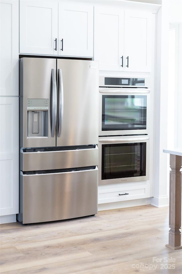 kitchen with stainless steel appliances, white cabinets, and light wood-type flooring