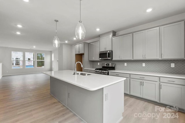 kitchen with sink, stainless steel appliances, an island with sink, decorative light fixtures, and gray cabinets