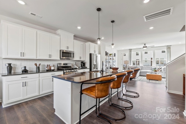 kitchen with stainless steel appliances, dark hardwood / wood-style floors, pendant lighting, a kitchen island with sink, and white cabinets