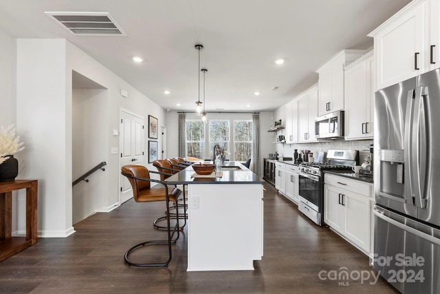 kitchen with white cabinets, appliances with stainless steel finishes, a kitchen island with sink, and pendant lighting