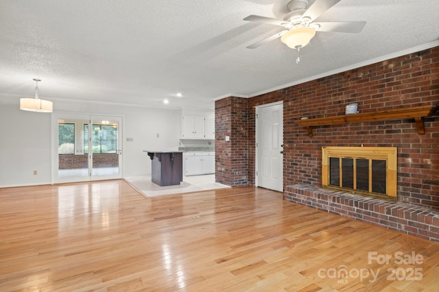 unfurnished living room with light wood-type flooring, ornamental molding, a textured ceiling, ceiling fan, and a fireplace