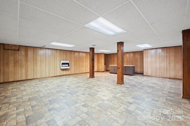 basement with heating unit, wood walls, and a drop ceiling