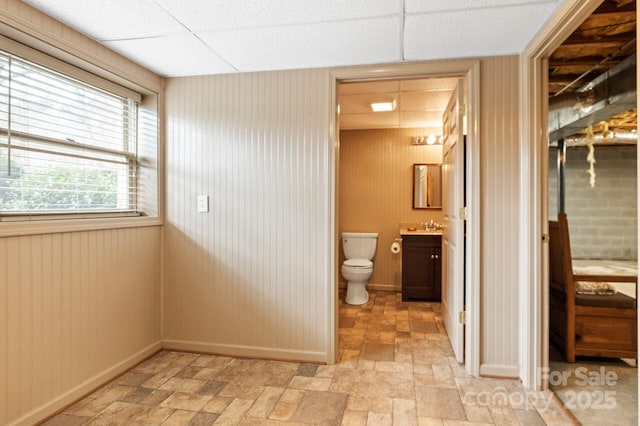 bathroom with wooden walls, a drop ceiling, toilet, and vanity