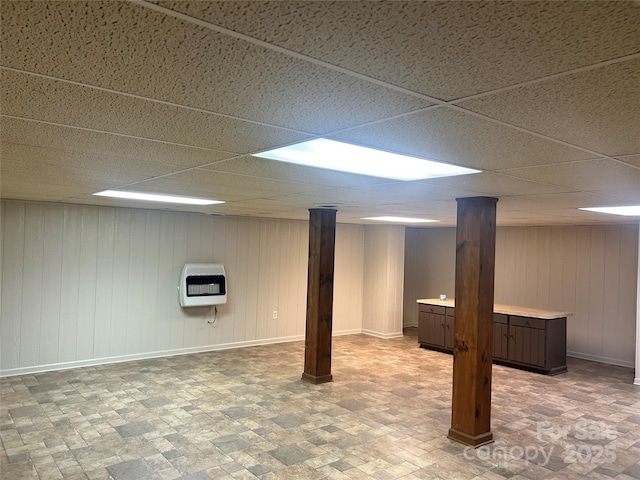 finished basement with baseboards, a drop ceiling, and heating unit