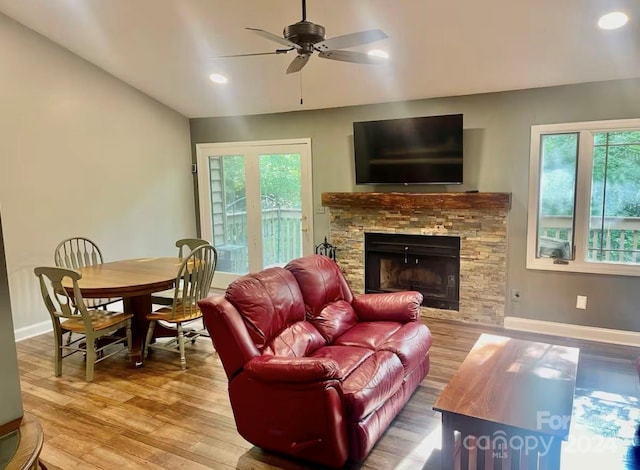 living room featuring vaulted ceiling, hardwood / wood-style flooring, a stone fireplace, and ceiling fan