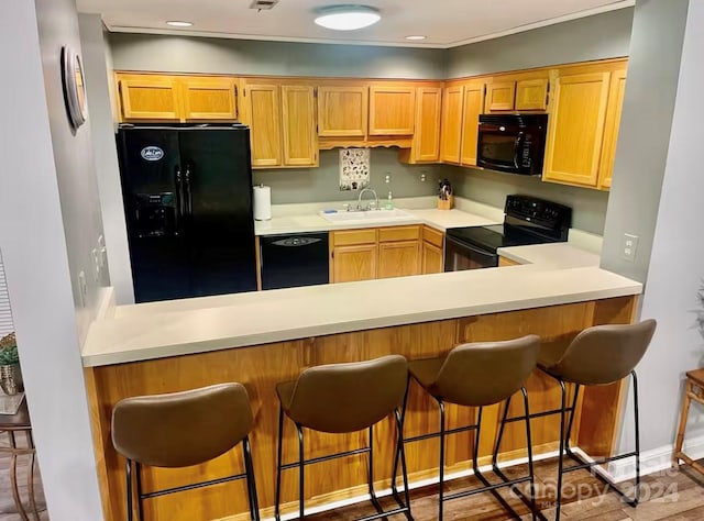 kitchen with black appliances, kitchen peninsula, sink, and a breakfast bar area