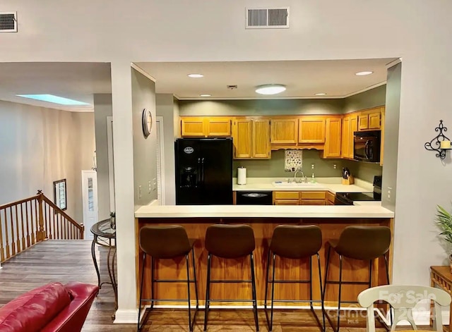 kitchen featuring dark wood-type flooring, black appliances, sink, a skylight, and a kitchen bar