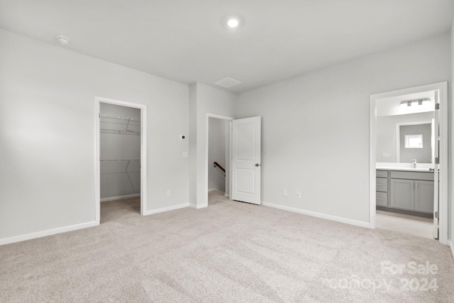 unfurnished bedroom with light carpet, sink, ensuite bath, a spacious closet, and a closet