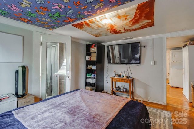 bedroom with hardwood / wood-style flooring, stacked washer / drying machine, white fridge, and ornamental molding