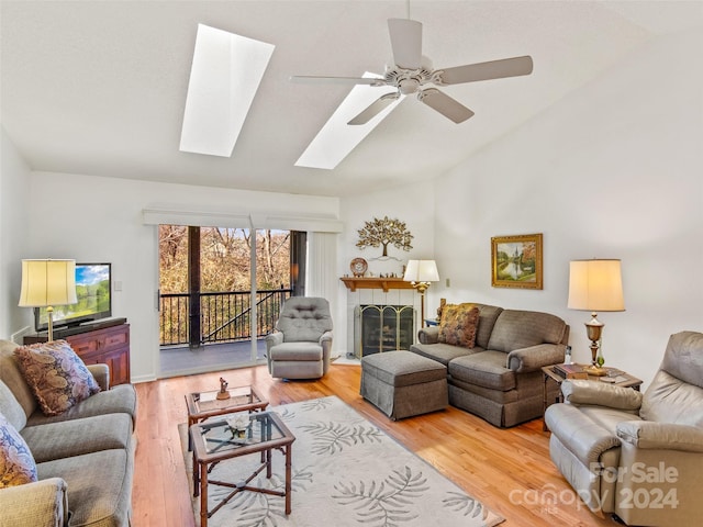 living room with a fireplace, hardwood / wood-style flooring, ceiling fan, and vaulted ceiling with skylight