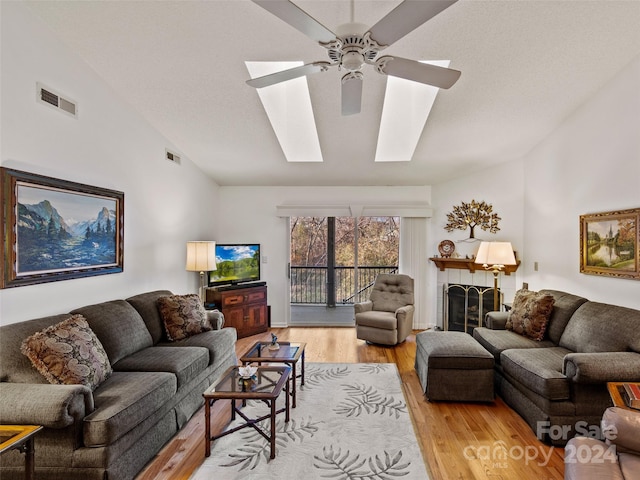 living room featuring a fireplace, light hardwood / wood-style floors, ceiling fan, and vaulted ceiling with skylight