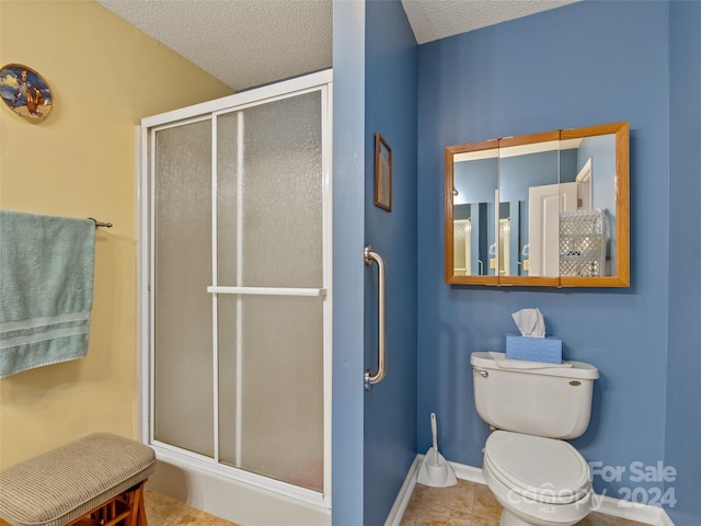 bathroom featuring tile patterned flooring, a textured ceiling, toilet, and a shower with shower door