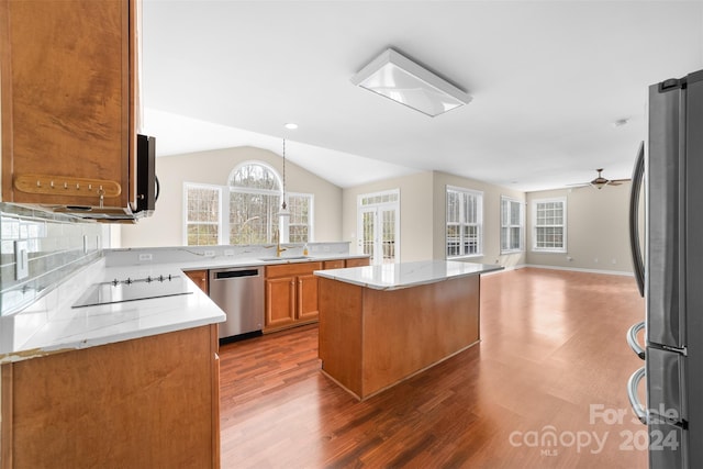 kitchen featuring appliances with stainless steel finishes, light stone counters, decorative light fixtures, dark hardwood / wood-style floors, and a kitchen island