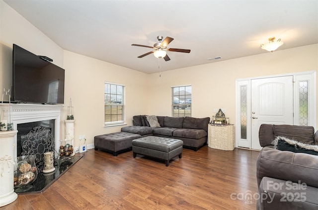 living room featuring a fireplace, ceiling fan, and dark wood-type flooring