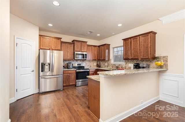 kitchen with dark wood-type flooring, decorative backsplash, light stone countertops, appliances with stainless steel finishes, and kitchen peninsula