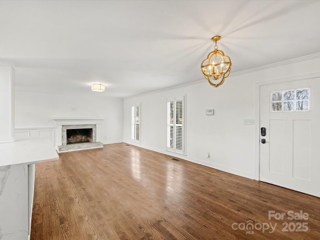 unfurnished living room featuring hardwood / wood-style floors, ornamental molding, and an inviting chandelier