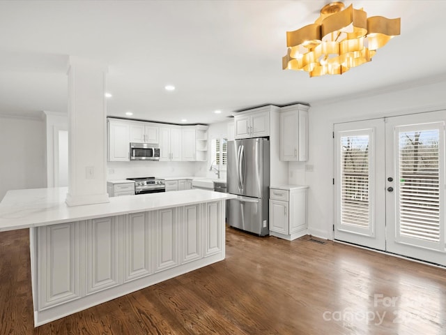 kitchen with dark hardwood / wood-style flooring, stainless steel appliances, crown molding, a notable chandelier, and white cabinets