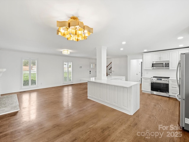 kitchen with ornamental molding, stainless steel appliances, hardwood / wood-style flooring, white cabinets, and a chandelier