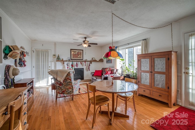 dining space featuring a brick fireplace, ceiling fan, a textured ceiling, and light wood-type flooring