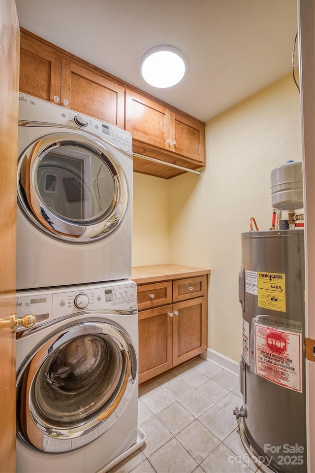 laundry area featuring cabinets, light tile patterned floors, electric water heater, and stacked washer and dryer