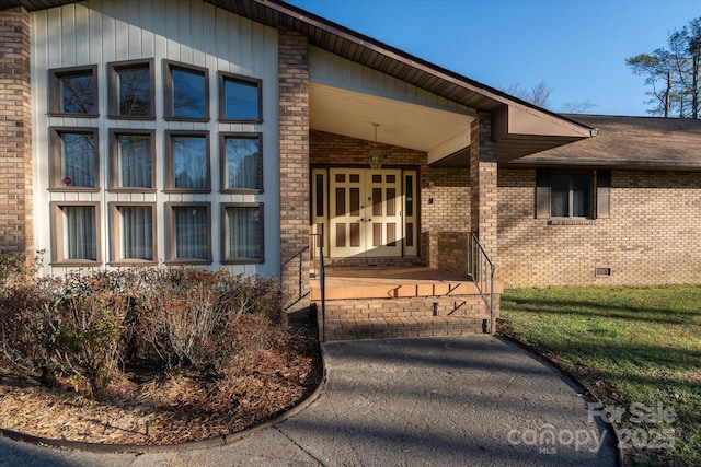 entrance to property with brick siding, crawl space, and a lawn