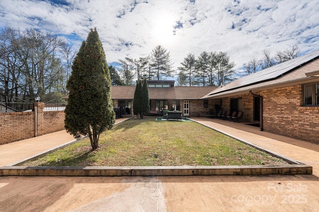 exterior space with a patio area, a front yard, fence, solar panels, and brick siding