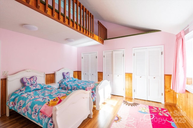 bedroom featuring two closets, wood finished floors, and a wainscoted wall