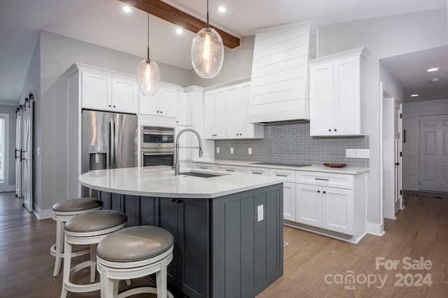 kitchen with a kitchen island with sink, sink, a barn door, decorative light fixtures, and white cabinets