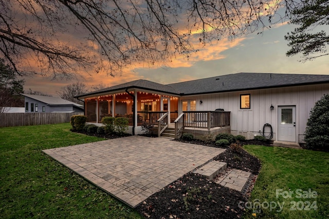 back house at dusk with a deck, a yard, and a patio