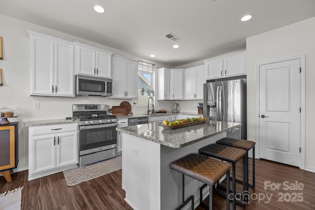 kitchen featuring appliances with stainless steel finishes, dark hardwood / wood-style flooring, a kitchen island, stone countertops, and white cabinetry