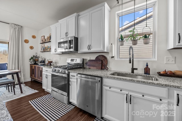 kitchen featuring sink, white cabinetry, light stone counters, appliances with stainless steel finishes, and pendant lighting