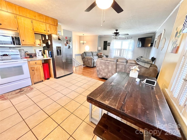 kitchen with a textured ceiling, light tile patterned floors, ceiling fan with notable chandelier, and appliances with stainless steel finishes