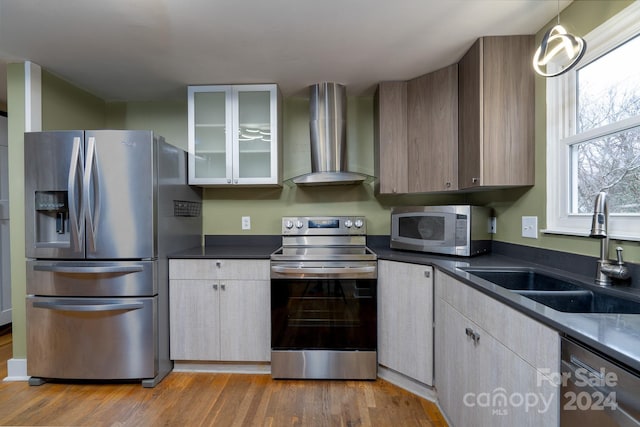 kitchen featuring pendant lighting, wall chimney range hood, sink, light hardwood / wood-style flooring, and appliances with stainless steel finishes