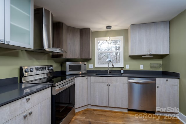 kitchen with sink, pendant lighting, appliances with stainless steel finishes, hardwood / wood-style flooring, and wall chimney range hood