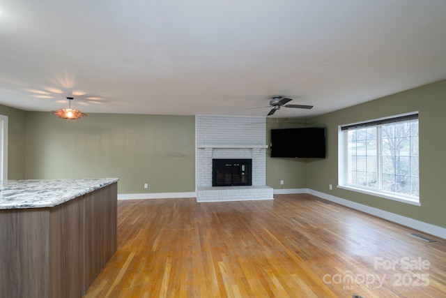 unfurnished living room with ceiling fan, a fireplace, and light hardwood / wood-style floors