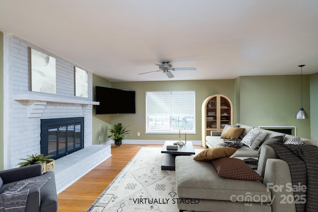 living room featuring ceiling fan, light hardwood / wood-style floors, and a brick fireplace