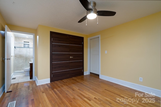 unfurnished bedroom featuring ceiling fan, ensuite bath, light hardwood / wood-style floors, and a textured ceiling