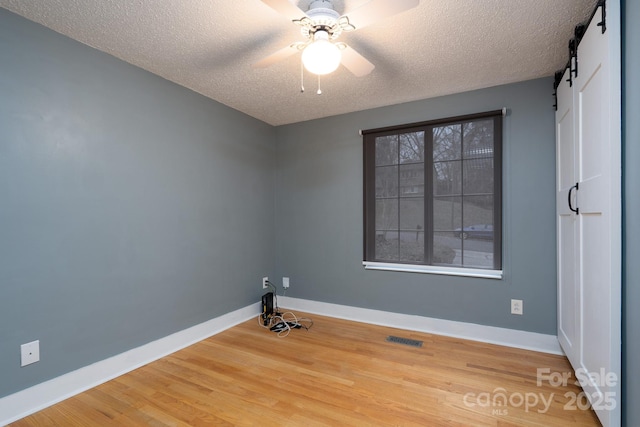 interior space featuring ceiling fan, wood-type flooring, a barn door, and a textured ceiling