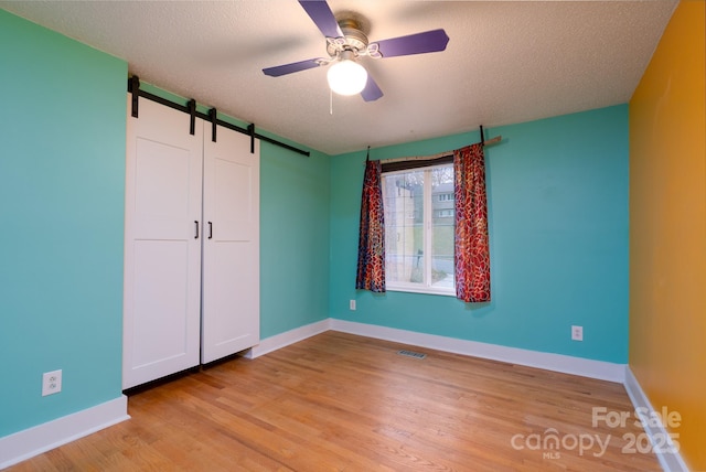 unfurnished bedroom with ceiling fan, a barn door, a textured ceiling, and light hardwood / wood-style floors