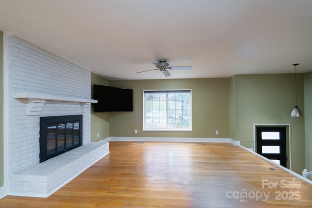 unfurnished living room featuring ceiling fan, hardwood / wood-style floors, and a brick fireplace