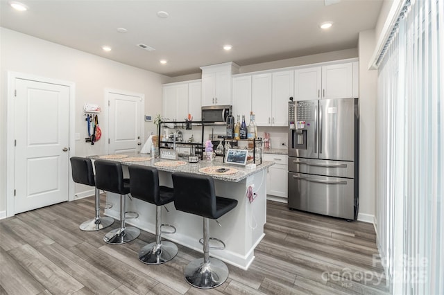 kitchen featuring white cabinets, light stone countertops, a kitchen island with sink, and appliances with stainless steel finishes