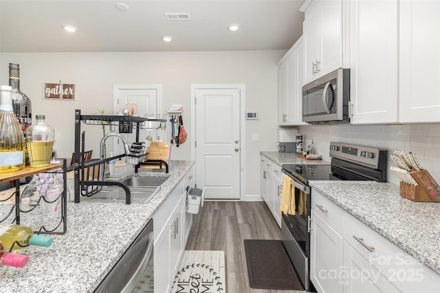 kitchen with backsplash, light stone counters, stainless steel appliances, sink, and white cabinetry